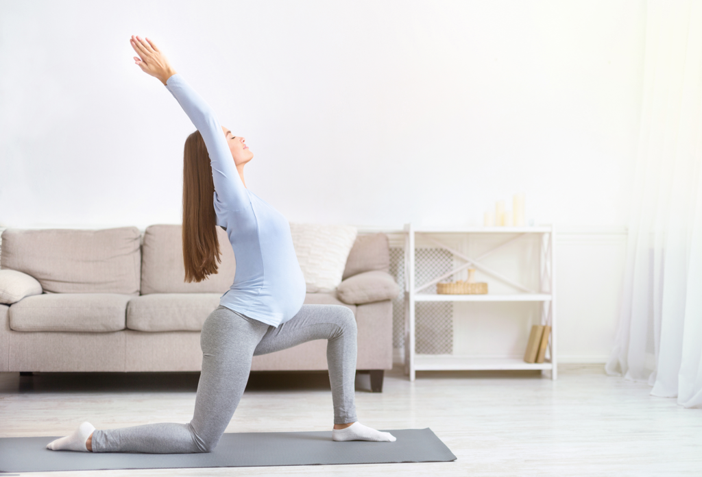 Schwangere Frau streckt ihre Arme nach oben bei Yogaübung.