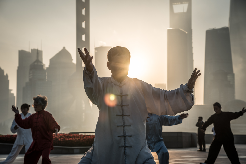 Ein älterer, asiatischer Mann praktiziert Tai Chi im Freien.